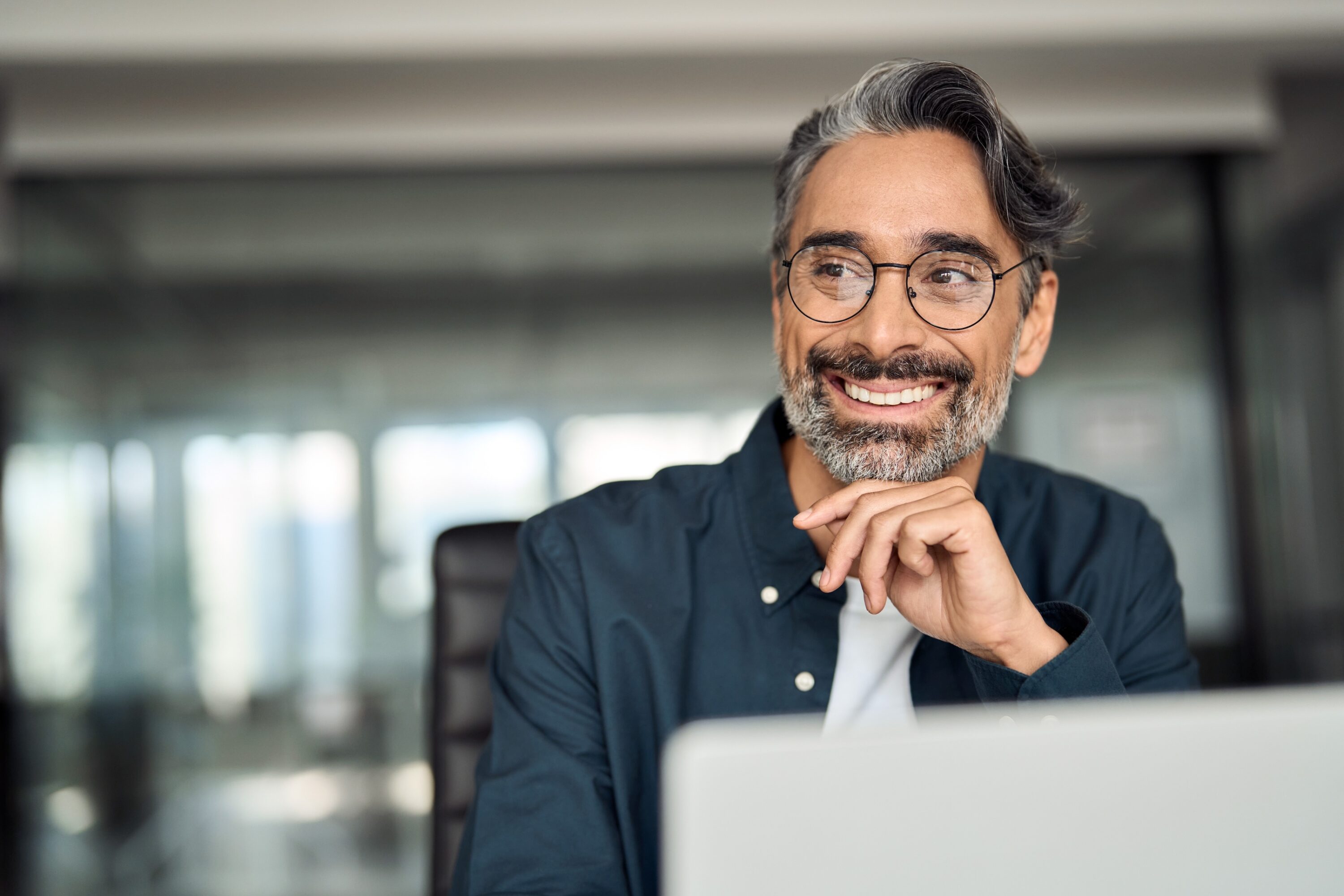 Smiling mature business man executive wearing shirt sitting at desk using laptop.